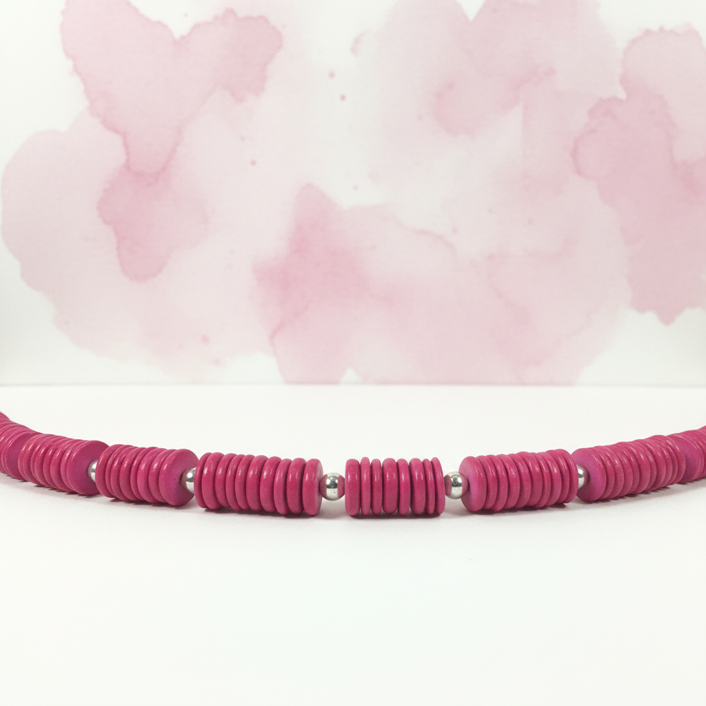 Close-up detail of pink coconut disk and silver beads on white surface with pink watercolor background
