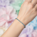 Blue topaz crystal tennis bracelet on model's wrist with light blurred background