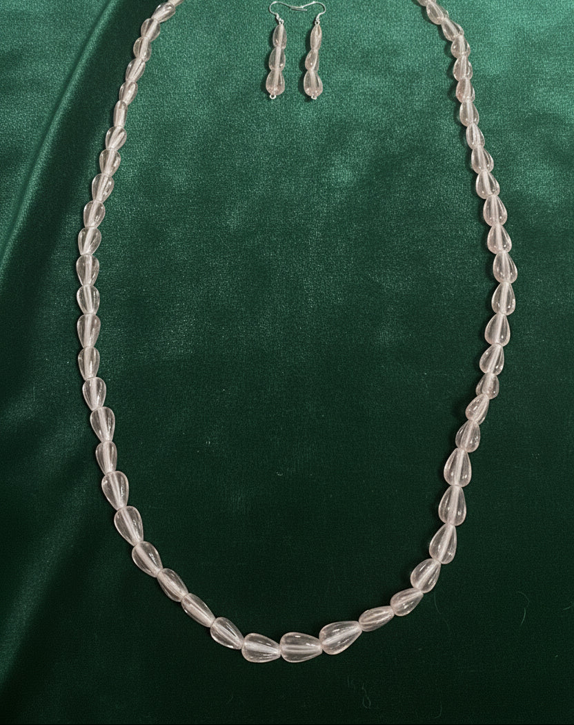 Pink faceted teardrop glass necklace set with matching elongated drop earrings on wood surface